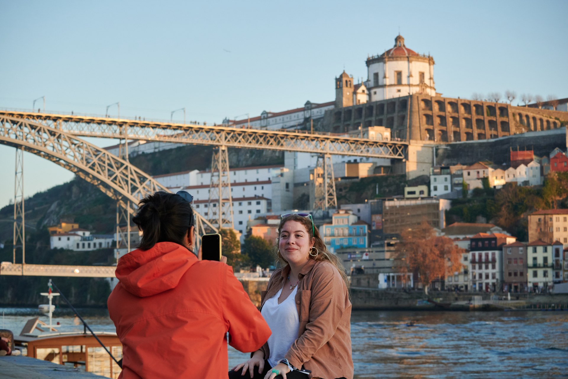 Porto’da bir köprünün önünde arkadaşının fotoğrafını çeken genç bir kadın